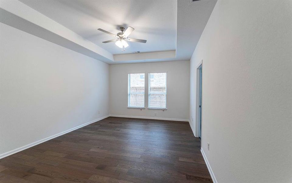 Spacious room featuring wood-finish flooring, a tray ceiling, and a ceiling fan
