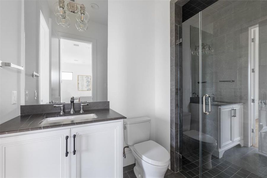 The fourth floor bathroom offers a gorgeous frameless glass walk-in shower, a rectangular under-mount sink, and an elongated commode. Shared between the bedroom and game room, this bathroom offers dual access points from both spaces. Image of a previously completed home in the community.