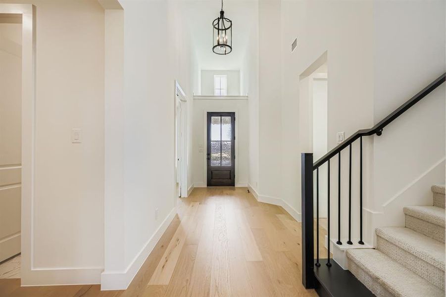 Foyer entrance with stairs, light wood-style flooring, a towering ceiling, and a chandelier Foyer entrance with stairs, light wood-style flooring, a towering ceiling, and a chandelier