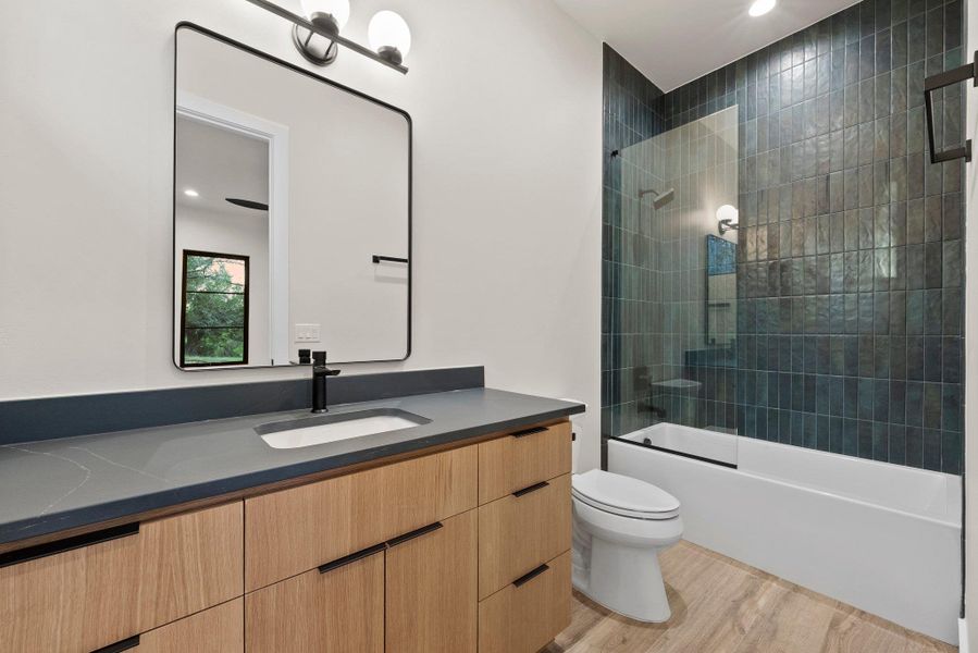 A well-appointed bathroom offers sleek vanity with dark countertop and modern fixtures, alongside a shower-tub combination featuring stylish dark tile surround.