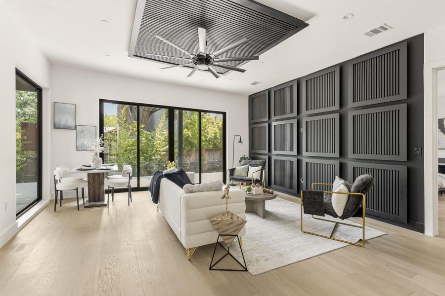 Spacious living area featuring light wood-finish flooring, a contemporary ceiling fan, and a striking black accent wall with decorative paneling