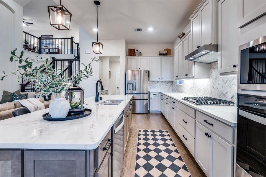 Kitchen with stainless steel appliances, white cabinetry, pendant lighting, and light stone countertops