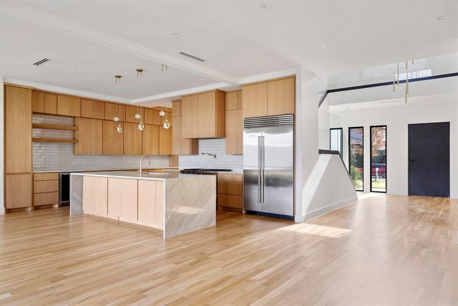 Kitchen featuring Luxury stainless steel built in fridge, decorative backsplash, light stone countertops, an island with sink, and open shelves Kitchen featuring Luxury stainless steel built in fridge, decorative backsplash, light stone countertops, an island with sink, and open shelves