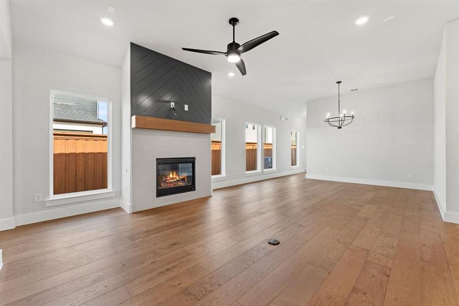 Unfurnished living room featuring lofted ceiling, a fireplace, ceiling fan with notable chandelier, and light hardwood / wood-style flooring