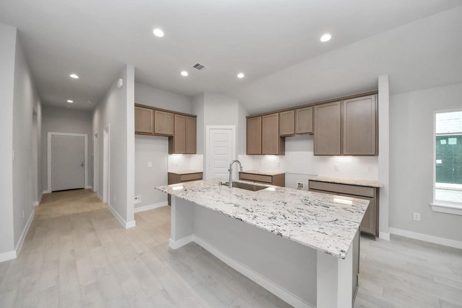 This generously spacious kitchen is a dream realized! With a massive granite island, high ceilings, soft close cabinets, granite countertops, stainless steel appliances, a sleek tile backsplash, recessed lighting, and an extended counter area. Sample photo of completed home with similar floor plan. Actual colors and selections may vary.
