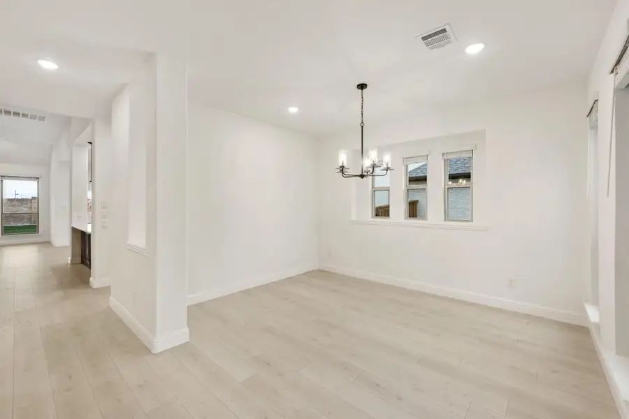 Empty dining room with light wood floors, white walls, and a black chandelier Empty dining room with light wood floors, white walls, and a black chandelier