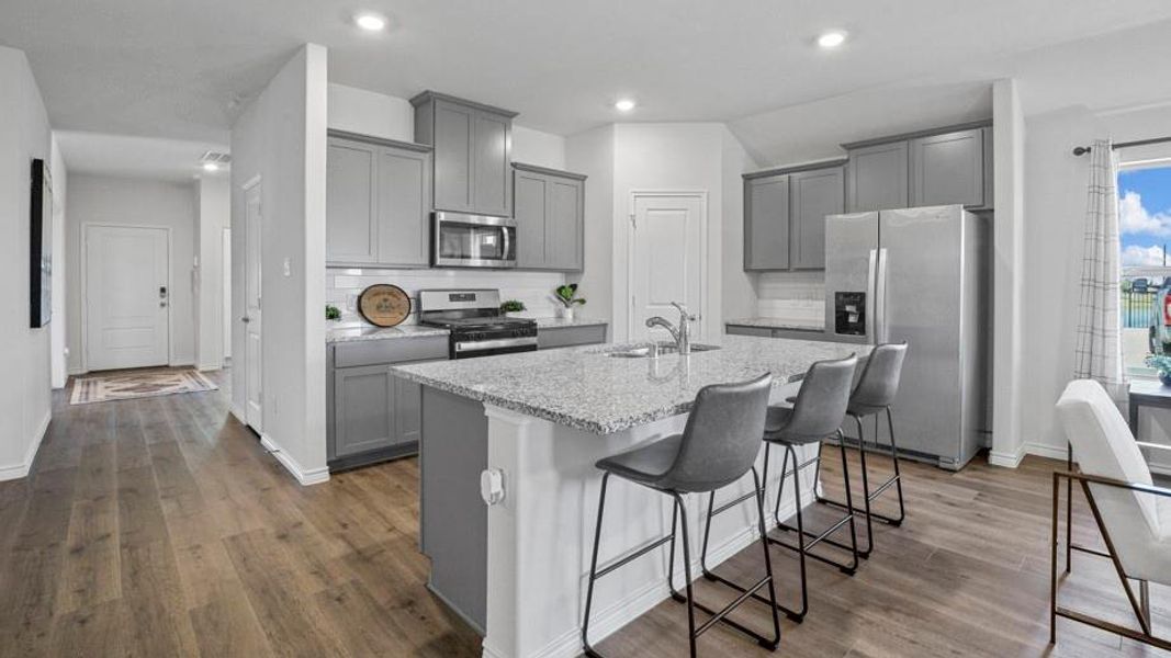 Kitchen featuring gray cabinets, appliances with stainless steel finishes, a breakfast bar, light stone counters, and recessed lighting