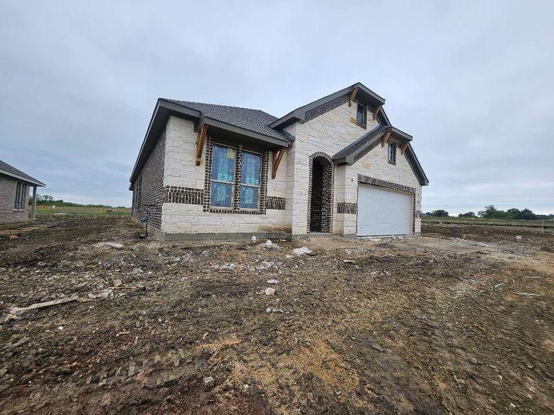Newly constructed home featuring a brick and stone exterior, an arched entryway, an attached garage, and decorative gable brackets Newly constructed home featuring a brick and stone exterior, an arched entryway, an attached garage, and decorative gable brackets
