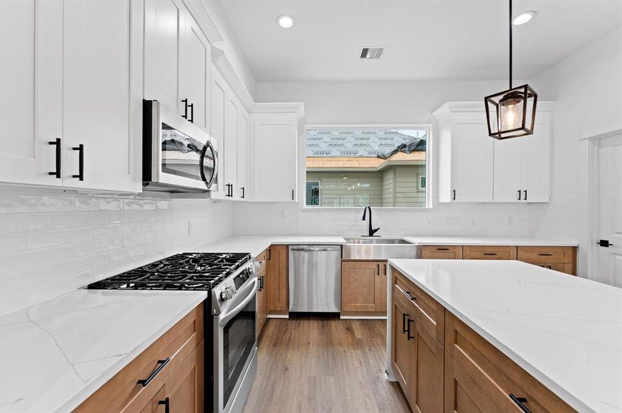 This modern kitchen features sleek white cabinets, a central island with quartz countertops, and stainless steel appliances. The space is bright and inviting, with a large window above the sink and stylish pendant lighting.