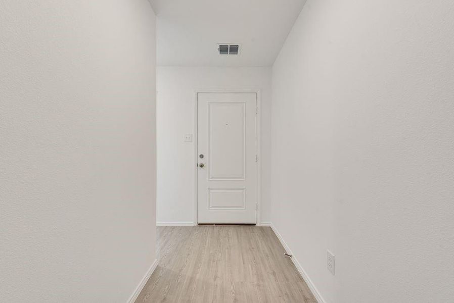 Hall featuring light wood-style floors, baseboards, and visible vents