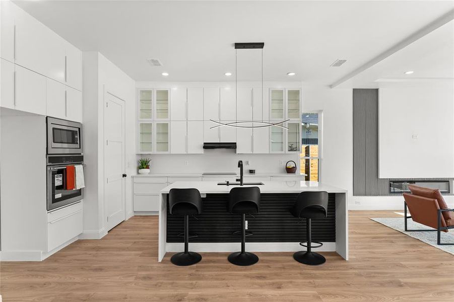 Kitchen with white cabinets, glass fronted cabinets, a breakfast bar, an island with sink, and light wood-type flooring