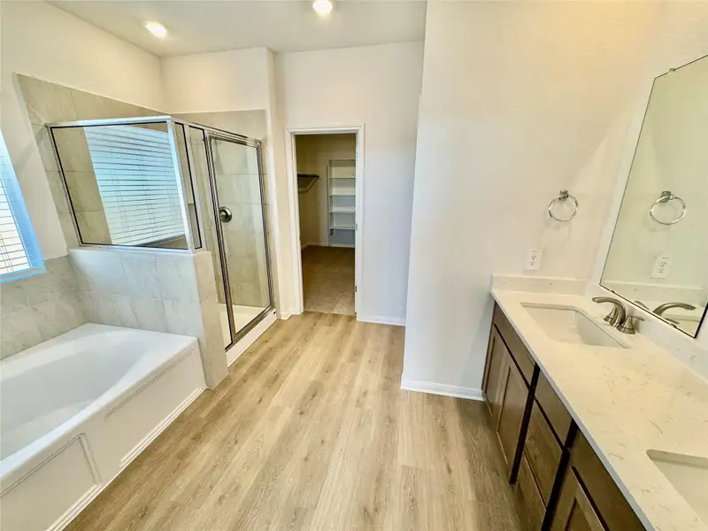 Bathroom with double vanity, light wood-type flooring, a spacious closet, a garden tub, and a shower stall Bathroom with double vanity, light wood-type flooring, a spacious closet, a garden tub, and a shower stall