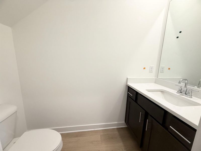 Half bathroom with toilet, vanity, wood finished floors, and baseboards Half bathroom with toilet, vanity, wood finished floors, and baseboards