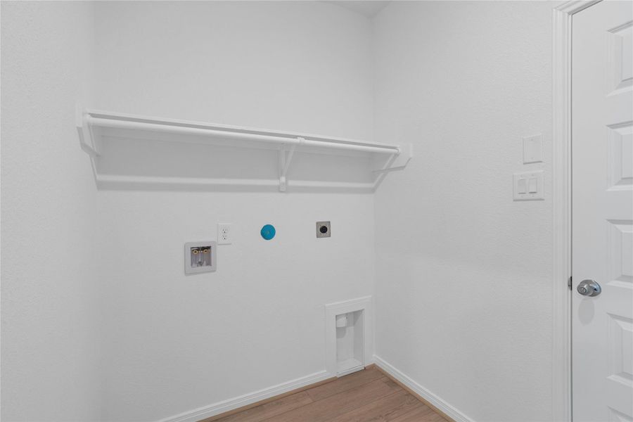 Dedicated laundry room equipped with full washer/dryer hookups, vinyl plank flooring, and a convenient overhead storage shelf with hanging rod.