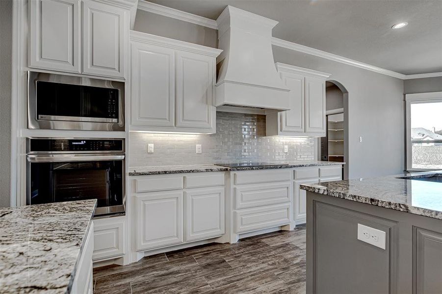 Kitchen with appliances with stainless steel finishes, premium range hood, white cabinetry, and ornamental molding