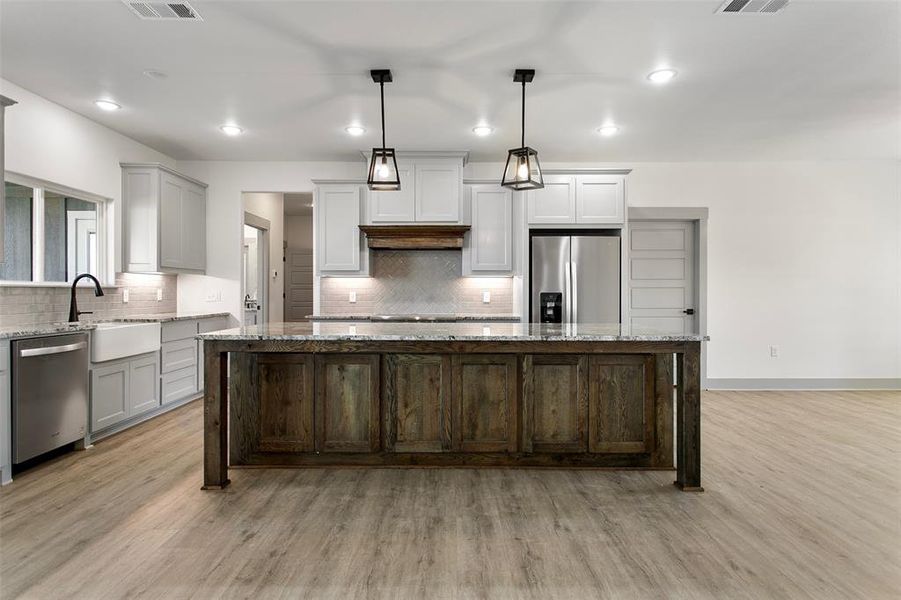 Kitchen featuring light stone counters, stainless steel appliances, dual tone cabinets, a center island, and decorative backsplash