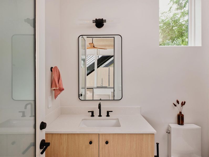 Contemporary bathroom featuring a light wood-finish vanity with black hardware, a rectangular undermount sink, and a white countertop