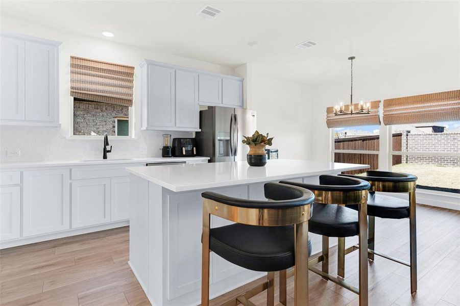 Kitchen featuring hanging light fixtures, stainless steel fridge with ice dispenser, a chandelier, a center island, and light wood-type flooring Kitchen featuring hanging light fixtures, stainless steel fridge with ice dispenser, a chandelier, a center island, and light wood-type flooring