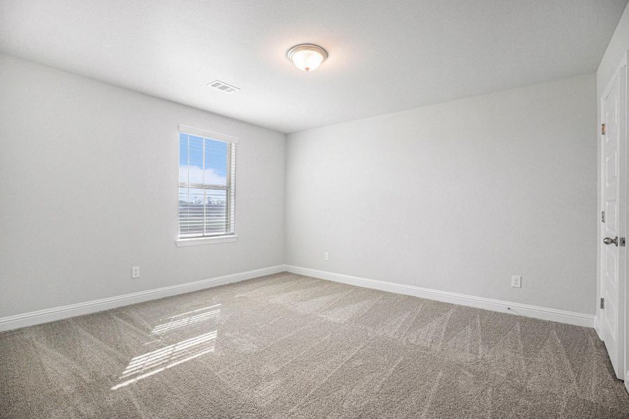 This is a bright, spacious room with neutral walls and carpeting, featuring a large window that lets in plenty of natural light. Ideal for a bedroom or home office.