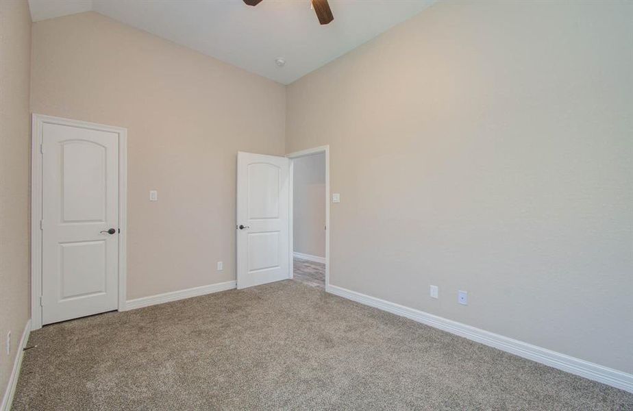 This is a clean, vacant room with neutral-colored walls and carpeted flooring, featuring two white doors and a ceiling fan. It is ready for personalization by the new homeowner.