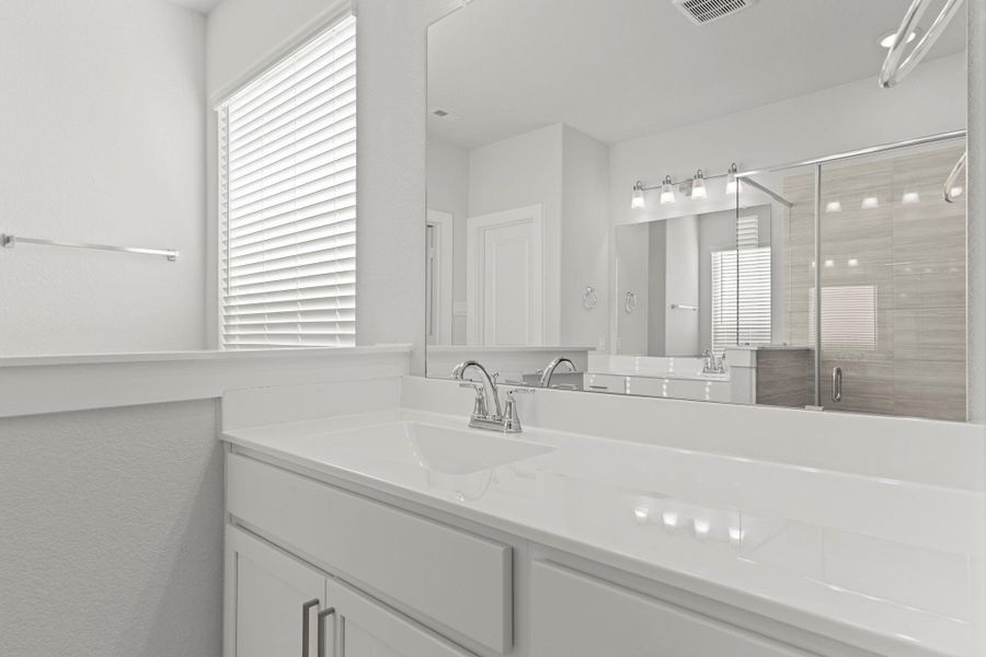 Another angle of the primary bath highlights the long, bright vanity area and open walkway leading toward the bedroom. Soft natural light and clean, neutral finishes create a refreshing and airy atmosphere.
