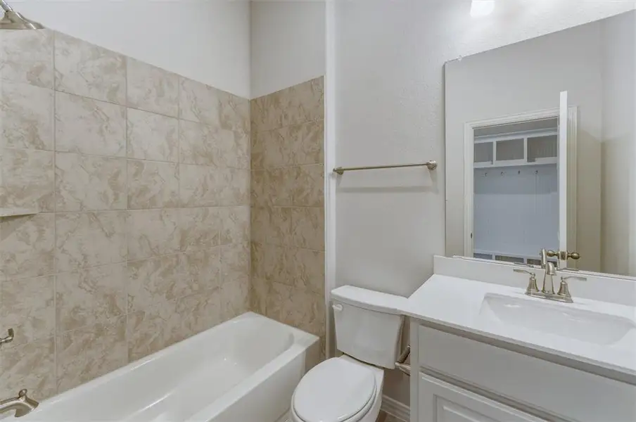 Bathroom featuring a white bathtub, beige tile surround, white vanity with integrated sink, brushed nickel faucet, and a large wall mirror Bathroom featuring a white bathtub, beige tile surround, white vanity with integrated sink, brushed nickel faucet, and a large wall mirror