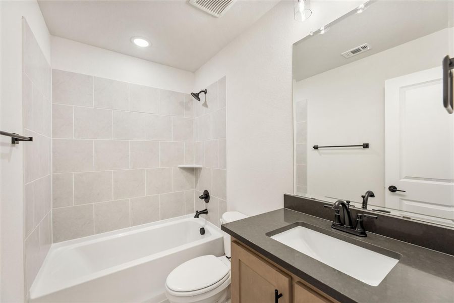 Bathroom with tiled tub-shower combo, dark countertop vanity, and black fixtures Bathroom with tiled tub-shower combo, dark countertop vanity, and black fixtures