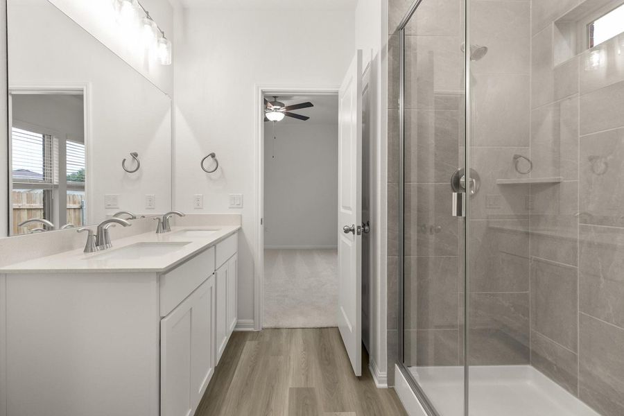 Bathroom featuring a double vanity with white cabinetry and a large mirror, alongside a shower with a glass enclosure and tiled walls