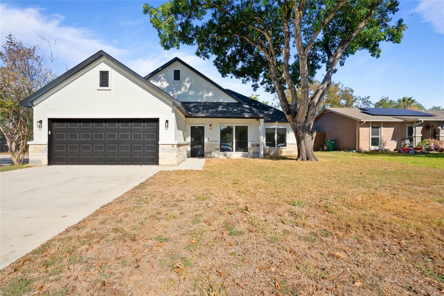 View of front facade featuring a front yard, stone siding, concrete driveway, and an attached garage