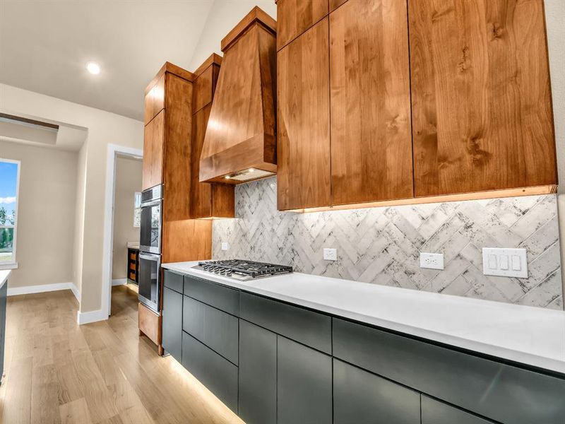 Kitchen featuring backsplash, premium range hood, stainless steel double oven, gas stovetop, and light hardwood / wood-style floors