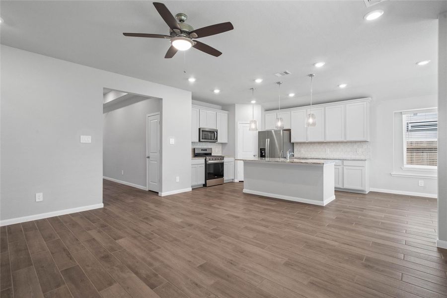 This expansive view from Great Room showcases a seamless, open-concept layout that creates a warm and inviting path for guests, drawing the eye toward the hallway leading to the secondary bedrooms and entry.
