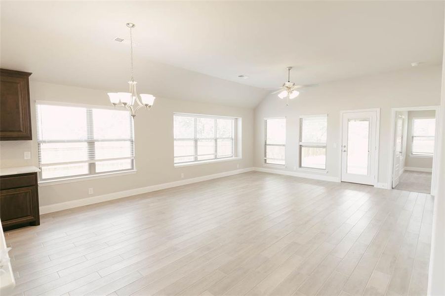 Unfurnished living room with light wood-type flooring, ceiling fan with notable chandelier, and vaulted ceiling