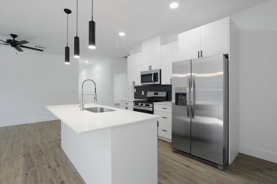 Kitchen featuring appliances with stainless steel finishes, sink, light hardwood / wood-style flooring, hanging light fixtures, and an island with sink