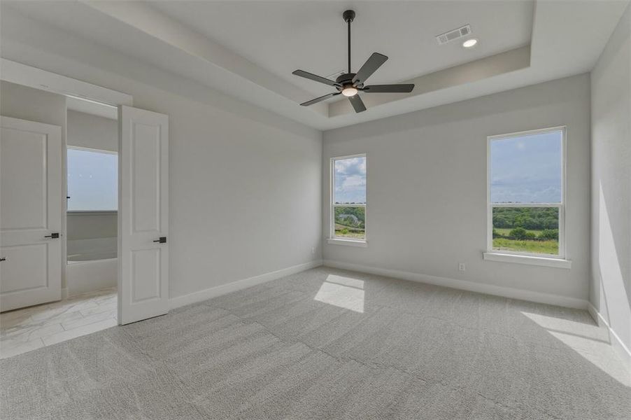 Spacious room featuring dual windows, tray ceiling, and a modern ceiling fan Spacious room featuring dual windows, tray ceiling, and a modern ceiling fan