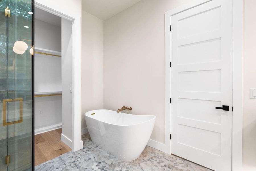 Freestanding soaking tub with gold-finish fixtures and patterned stone flooring