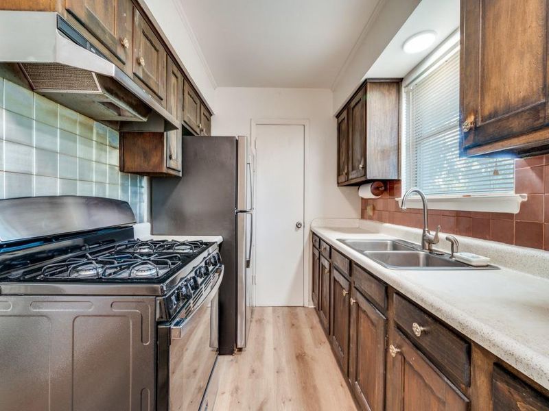Kitchen with stainless steel range with gas cooktop, light wood-style floors, under cabinet range hood, backsplash, and crown molding Kitchen with stainless steel range with gas cooktop, light wood-style floors, under cabinet range hood, backsplash, and crown molding