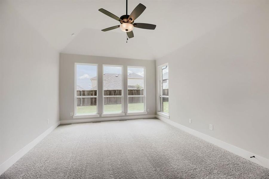 Spacious room featuring light gray carpet, multiple large windows, and a ceiling fan with integrated lighting