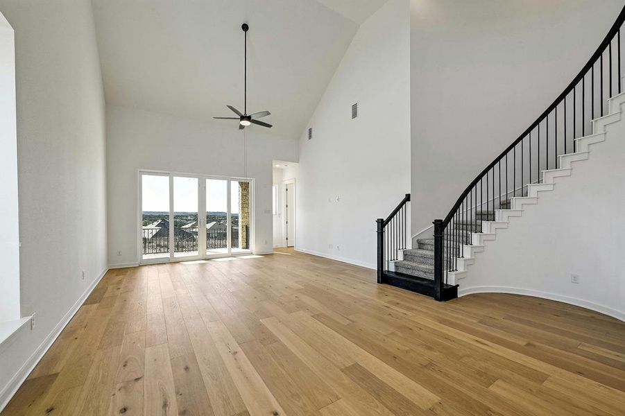Unfurnished living room featuring high vaulted ceiling, stairs, ceiling fan, and light wood finished floors