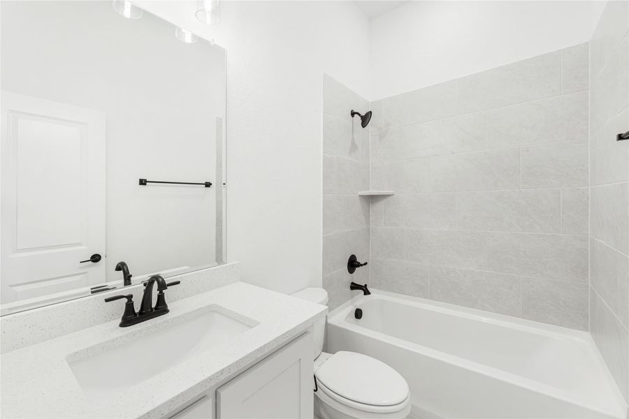 Bathroom with white vanity, quartz countertop, tub-shower combo with gray tile, and black fixtures