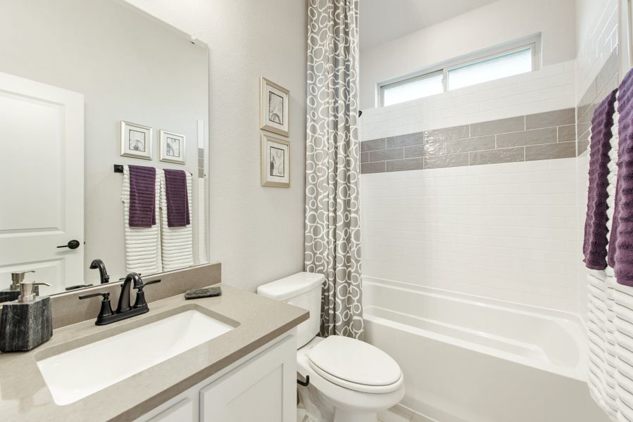 Full bathroom with white vanity, gray countertop, tub-shower combo, and tiled surround with accent strip Full bathroom with white vanity, gray countertop, tub-shower combo, and tiled surround with accent strip