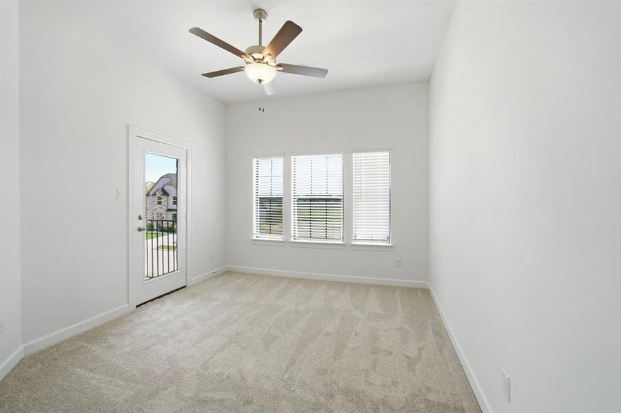 Bright room with plush carpeting, featuring three windows with blinds for natural light, a glass-paneled door opening to a small balcony, and a ceiling fan with integrated lighting Bright room with plush carpeting, featuring three windows with blinds for natural light, a glass-paneled door opening to a small balcony, and a ceiling fan with integrated lighting