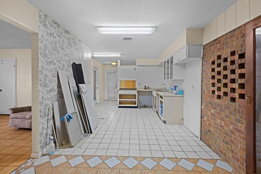 Kitchen with light countertops, light tile patterned floors, brick wall, and glass insert cabinets