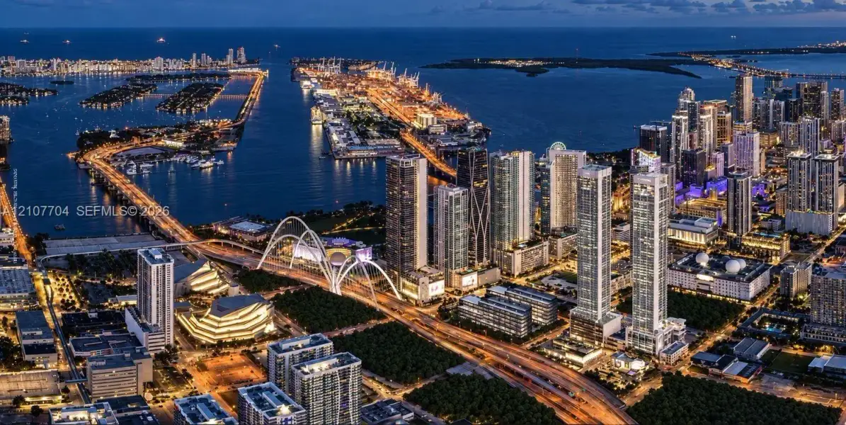 Aerial perspective of a metropolitan skyline featuring high-rise architecture, proximity to a coastal waterway, complex bridge infrastructure, and dense urban development