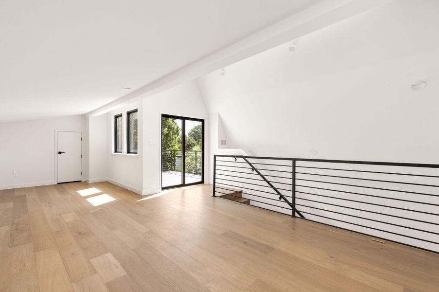 An airy, sun-filled loft space featuring light hardwood flooring and modern railing, opening to a tranquil balcony.