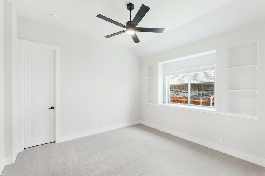 Empty bedroom with vaulted ceiling, black ceiling fan, built-in shelves, and carpet flooring Empty bedroom with vaulted ceiling, black ceiling fan, built-in shelves, and carpet flooring