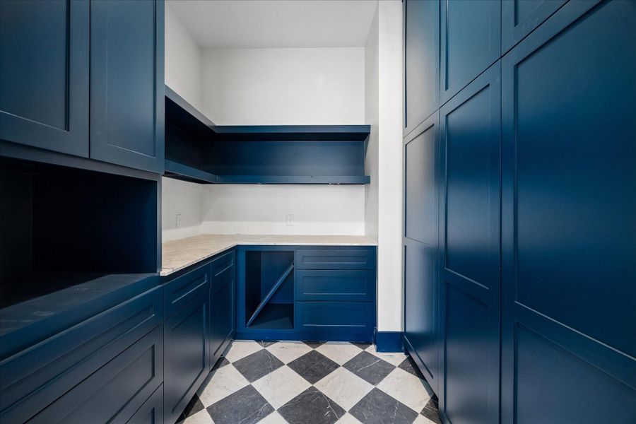 Striking utility or secondary prep space featuring custom floor to ceiling cabinetry in a bold deep blue finish, paired with contrasting light countertops for a clean, tailored look. Thoughtfully designed with ample storage, workspace, and upper shelving, this area is ideal for organization, hobbies, or additional kitchen support. The patterned tile flooring adds a sophisticated design element, elevating both style and functionality.