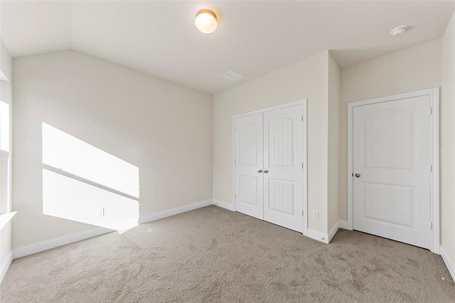 Unfurnished bedroom featuring light colored carpet, a closet, and lofted ceiling