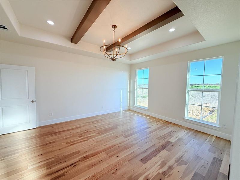 Empty room featuring a raised ceiling, suspended lighting, light wood-style floors, and beamed ceiling Empty room featuring a raised ceiling, suspended lighting, light wood-style floors, and beamed ceiling