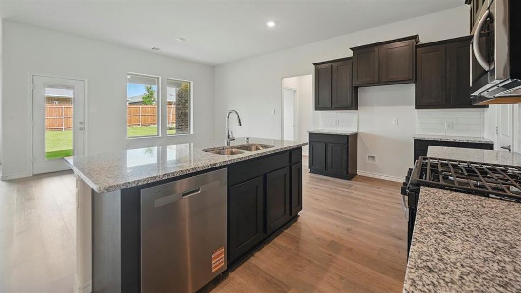 Kitchen featuring light stone counters, stainless steel appliances, light wood-style floors, decorative backsplash, and a center island with sink