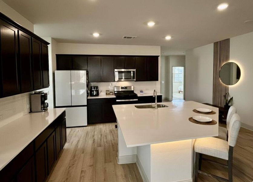 Kitchen featuring appliances with stainless steel finishes, light wood-type flooring, recessed lighting, a center island with sink, and a breakfast bar